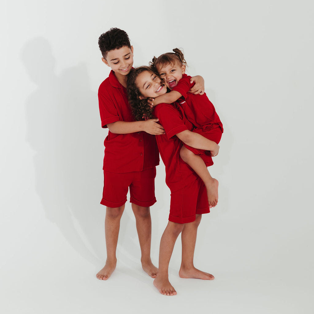 Three children in red outfits hugging each other on a white background