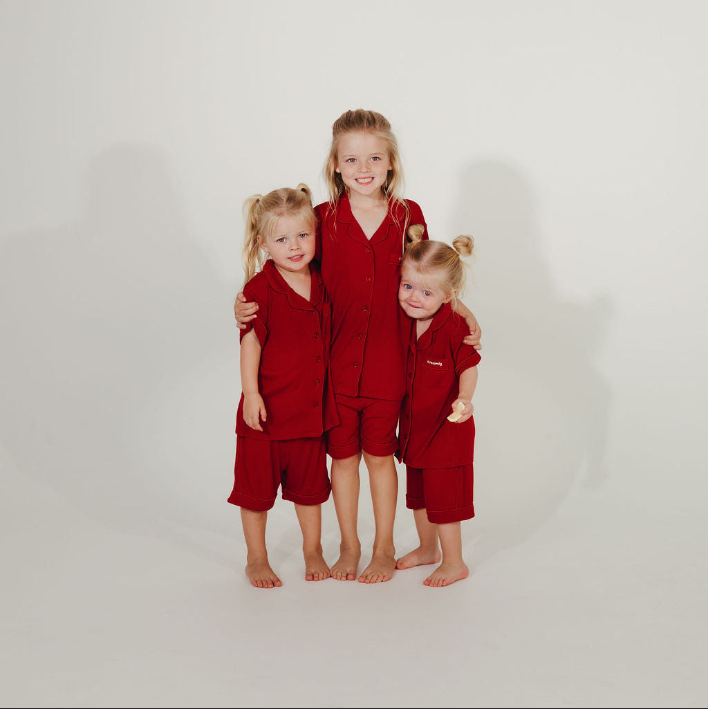 Three children in matching red outfits standing together on a white background